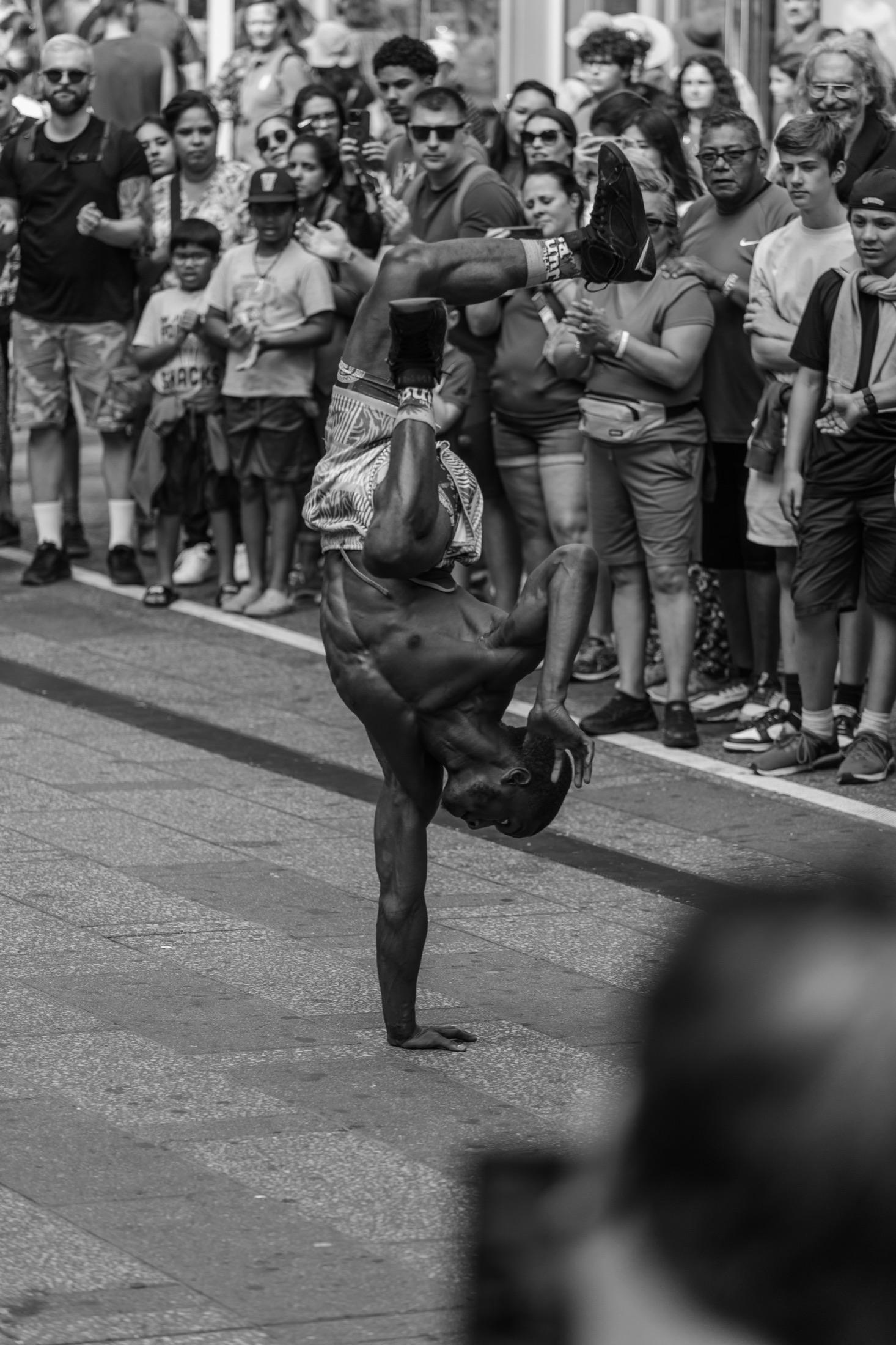 Breakdancer performing a one-arm handstand for a street crowd, black and white — street photography by Brian Mullin, New York City