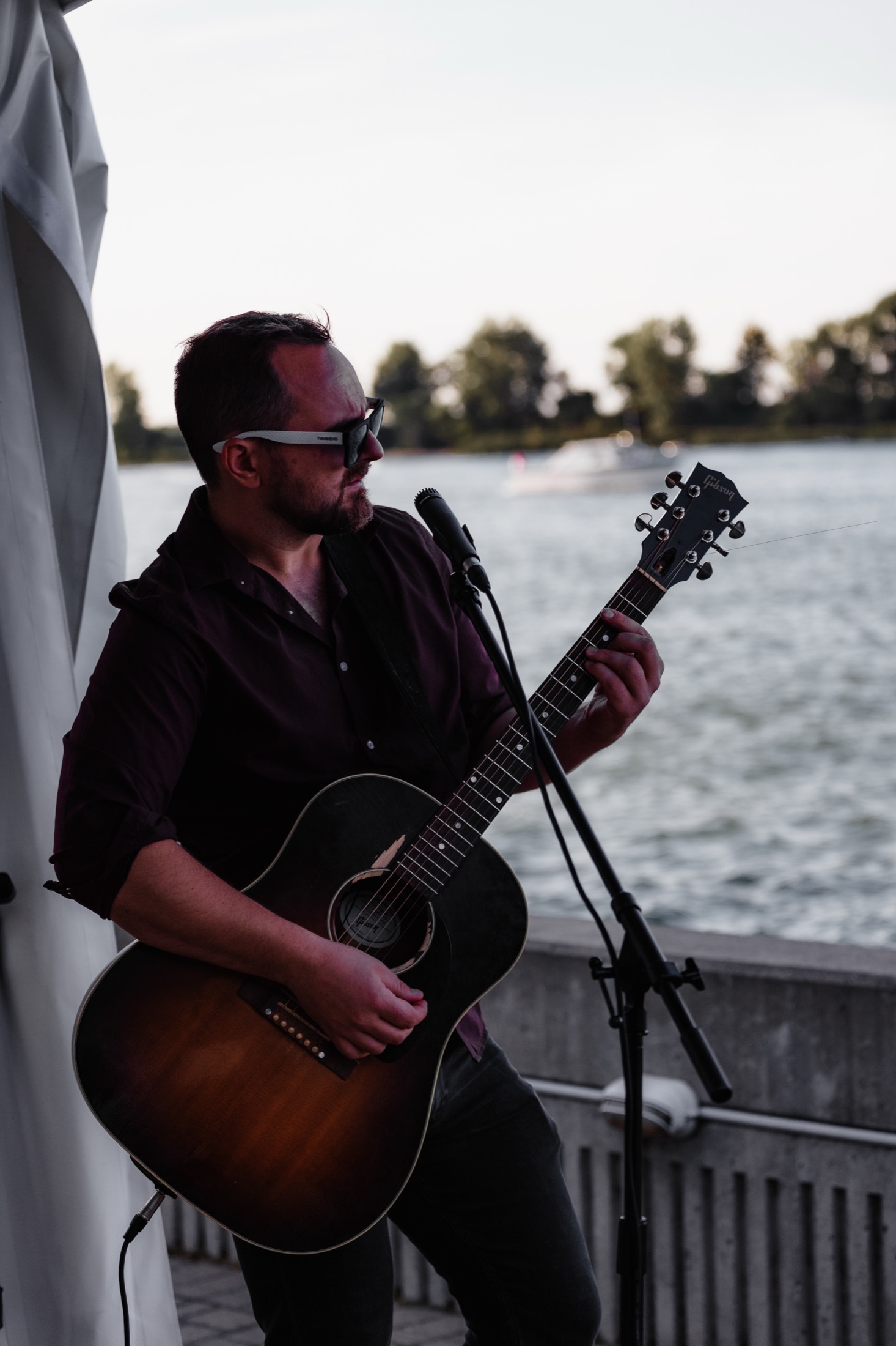 Guitarist performing at golden hour by the waterfront, warm tones — brand photography by Brian Mullin, Windsor