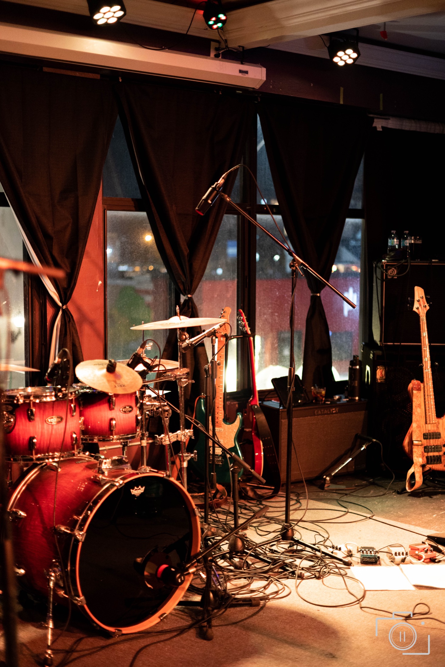 Red drum kit on stage with black drapes and city windows at night — brand photography by Brian Mullin, Pause Studios