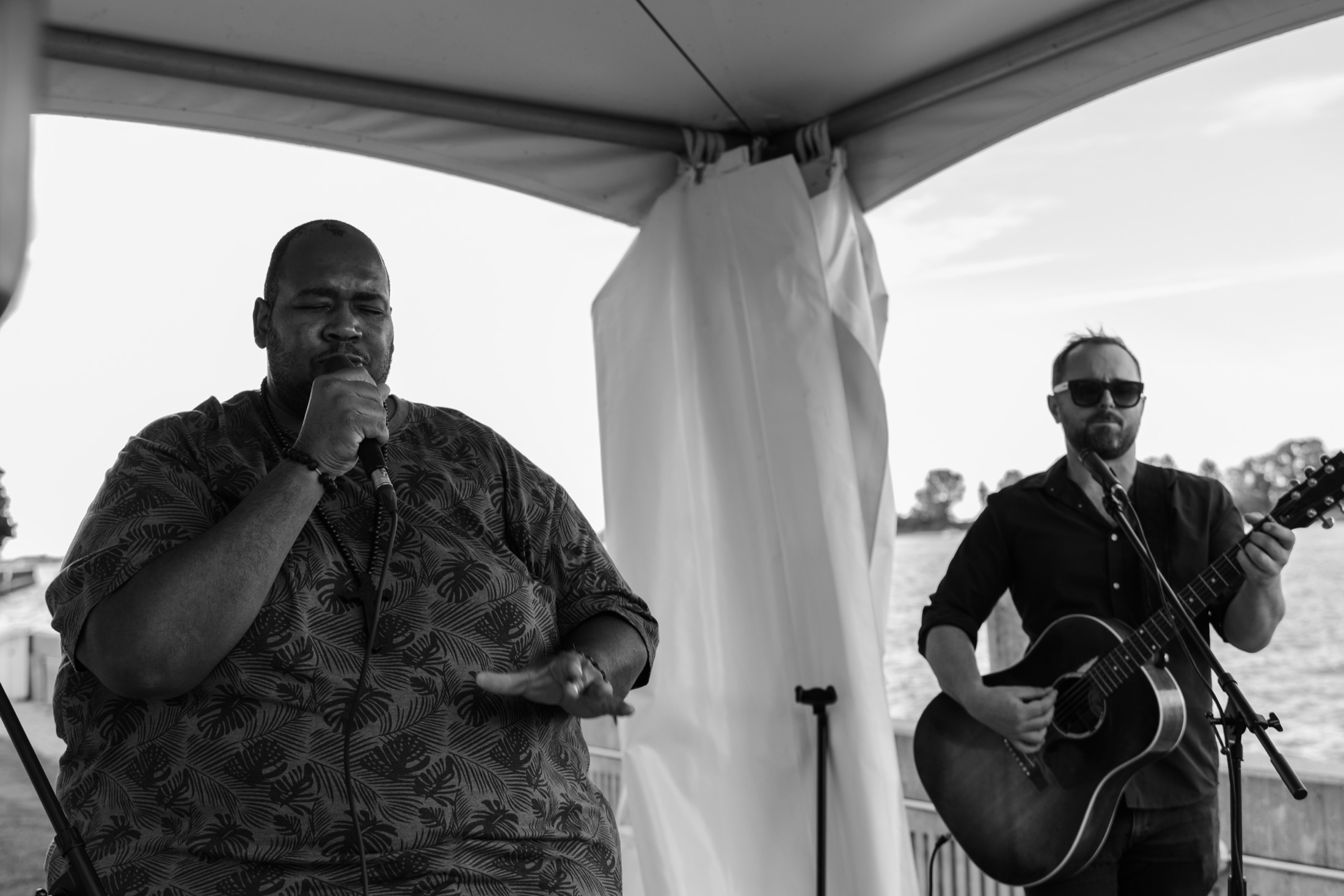 Vocalist and guitarist performing on an outdoor waterfront stage at dusk, black and white — event photography by Brian Mullin, Windsor