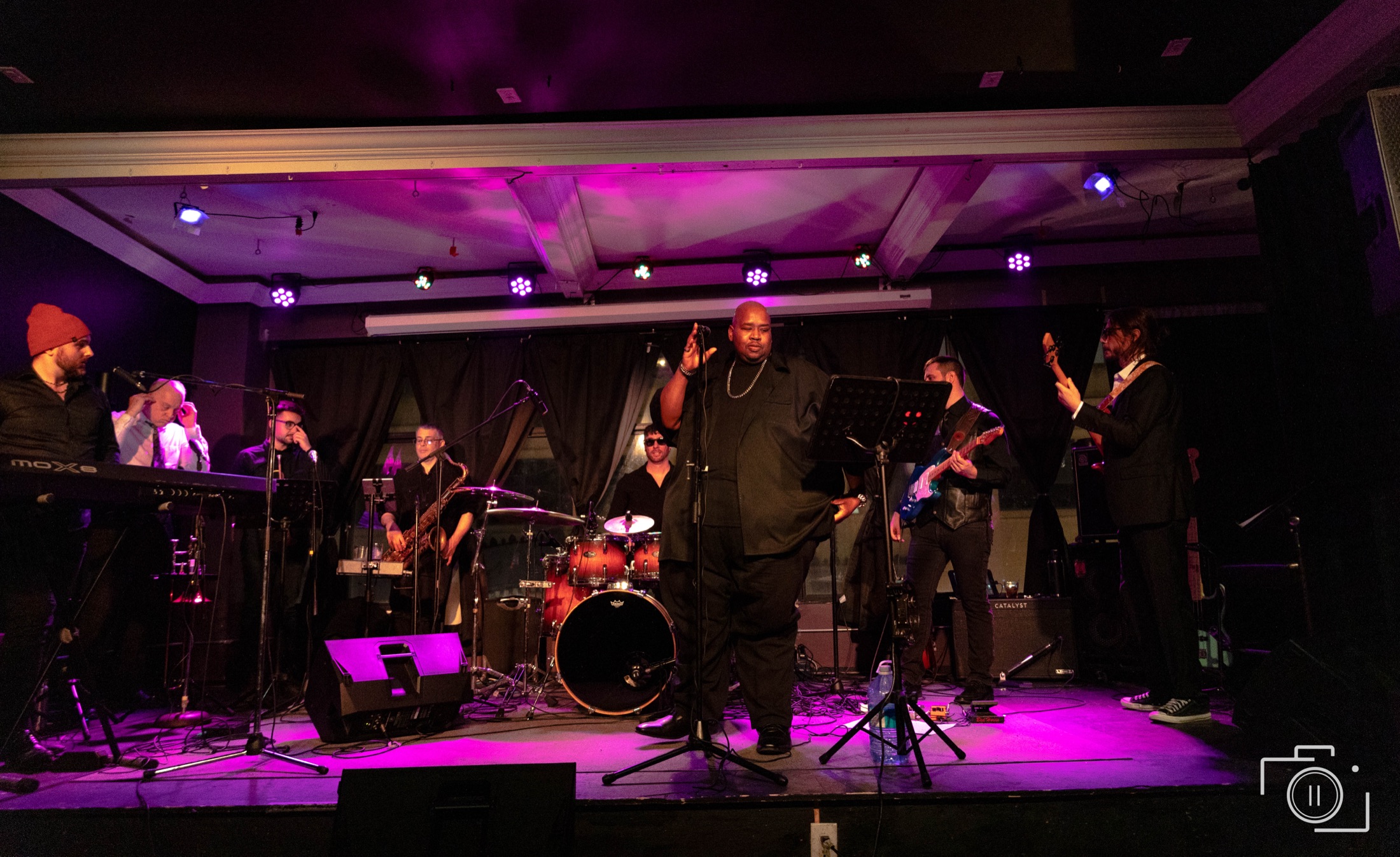 Full band on stage with purple stage lighting, vocalist commanding the room — live event photography by Brian Mullin