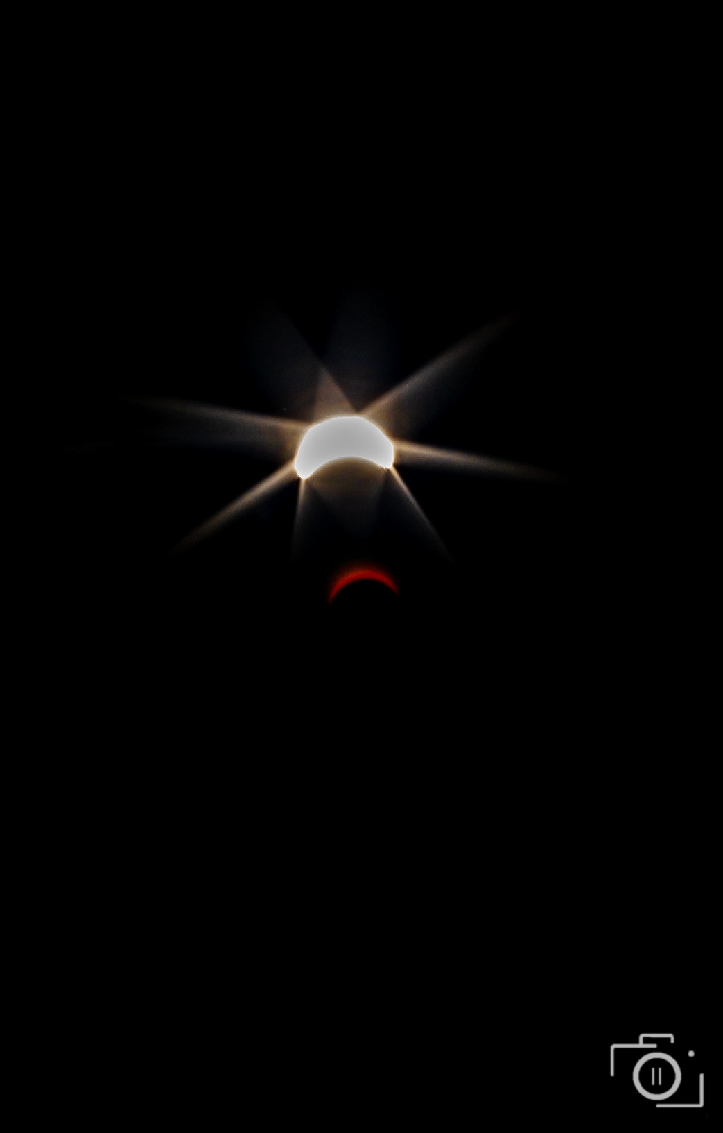 A partially eclipsed sun with a natural starburst flare and red crescent on a black sky — 2024 solar eclipse, editorial photography by Brian Mullin, Pause Studios.