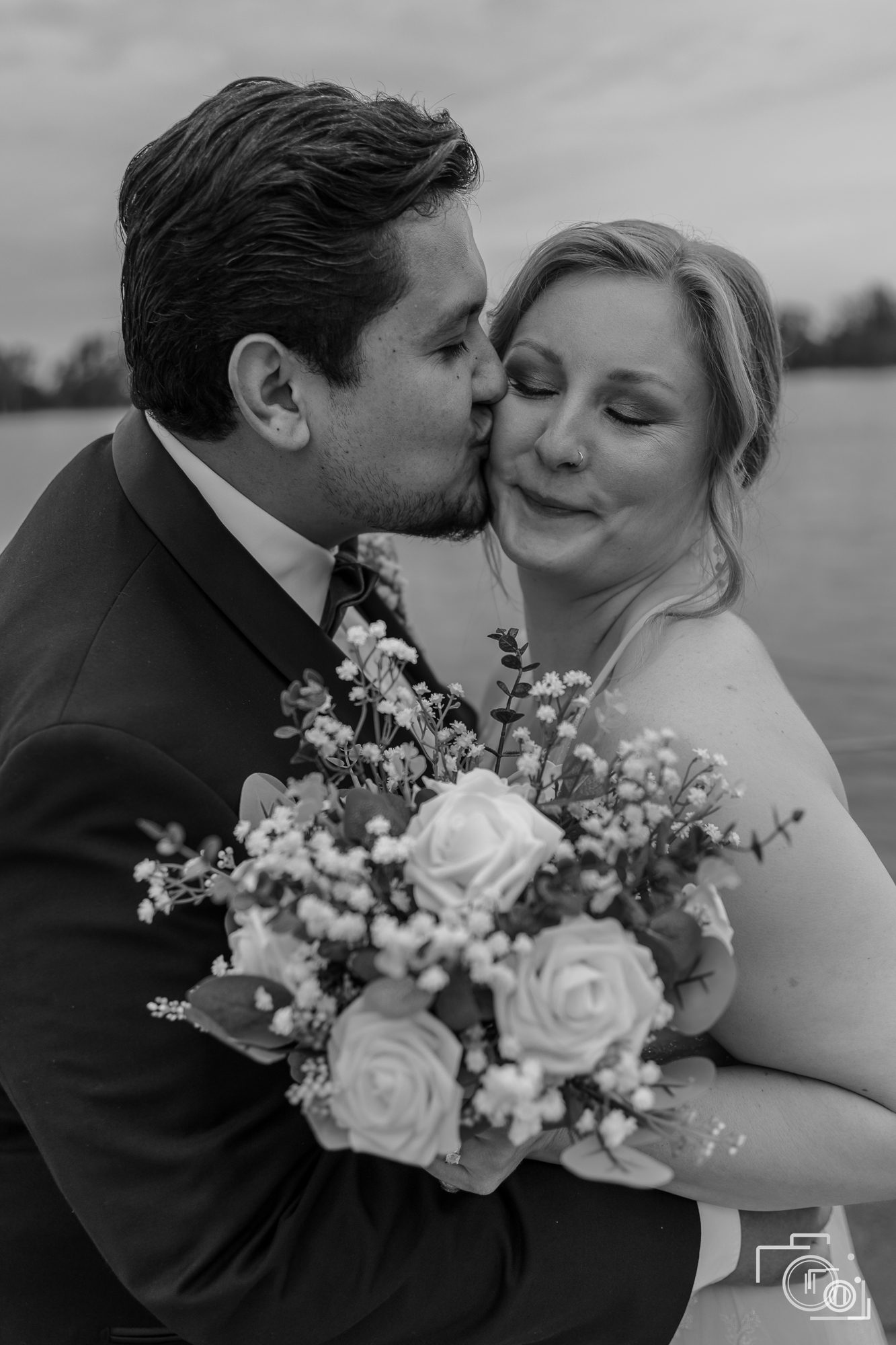 Groom kisses a laughing bride holding her bouquet, black and white. Candid wedding photography, Pause Studios.