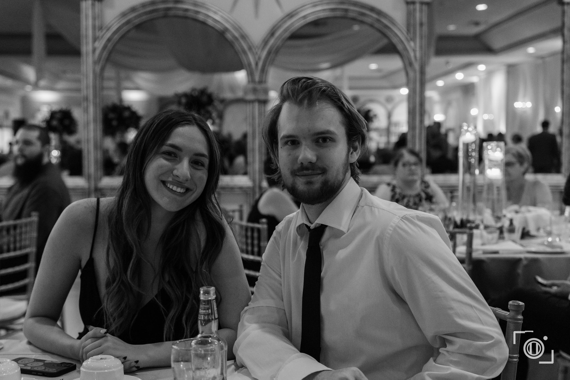 Couple sharing a quiet laugh at their table, black and white. Documentary wedding photography, Pause Studios.